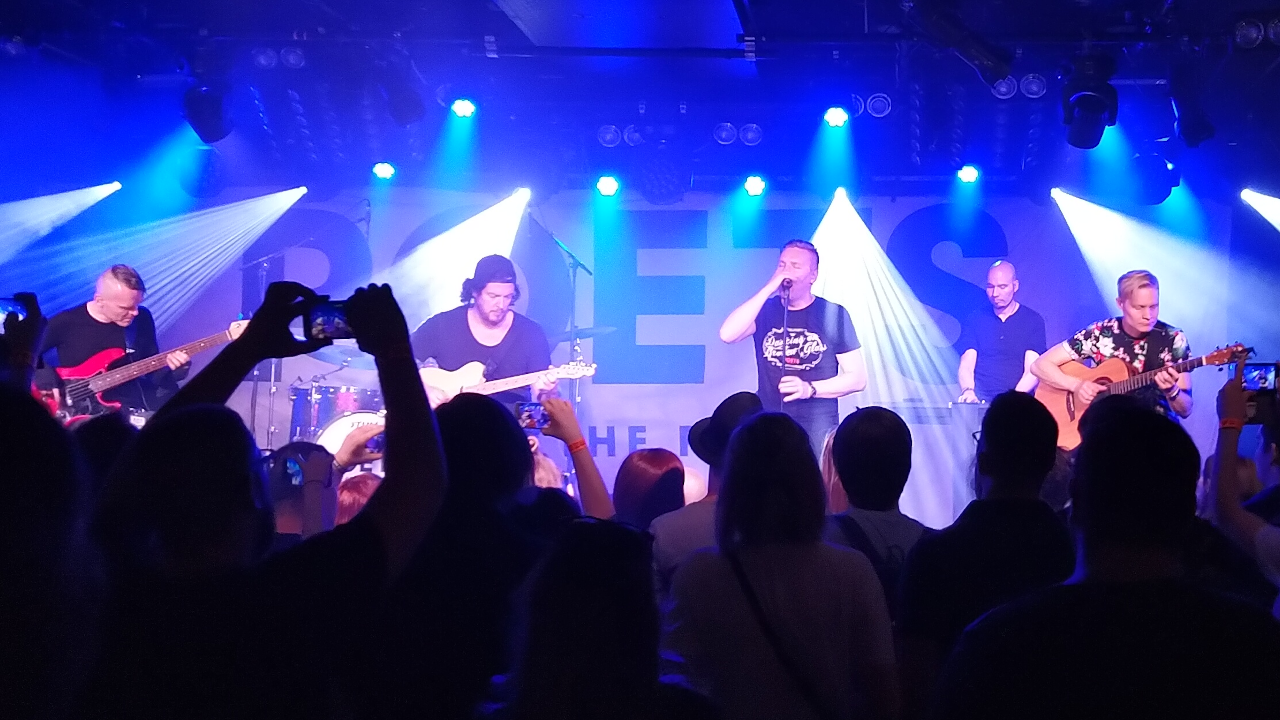 My own photo taken on the Ultraviolet concert. The band plays in the background illuminated by bright deep blue lights. In the front there are black silhuettes of people listening to them.